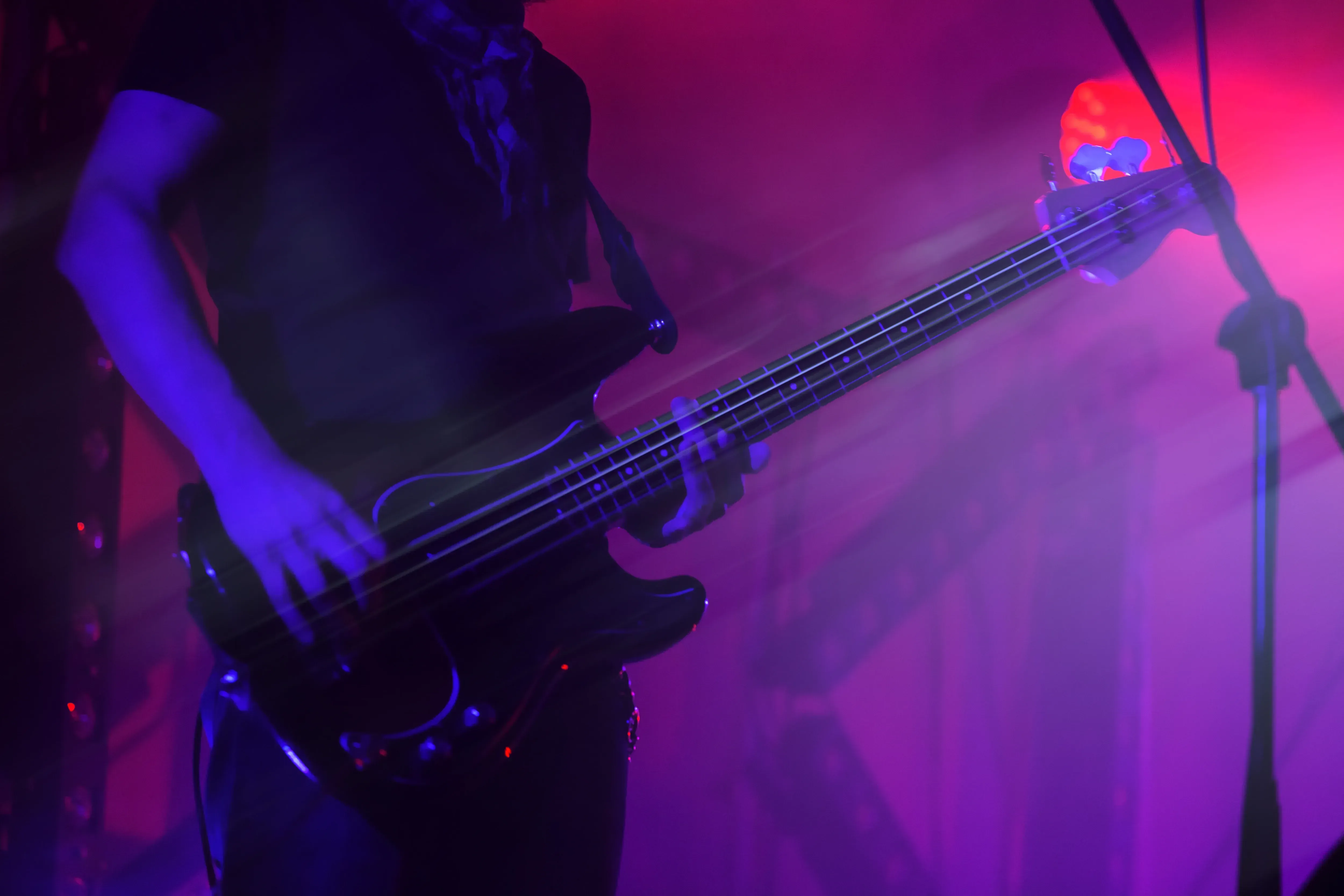 Bass guitarist performing on stage under purple lighting.