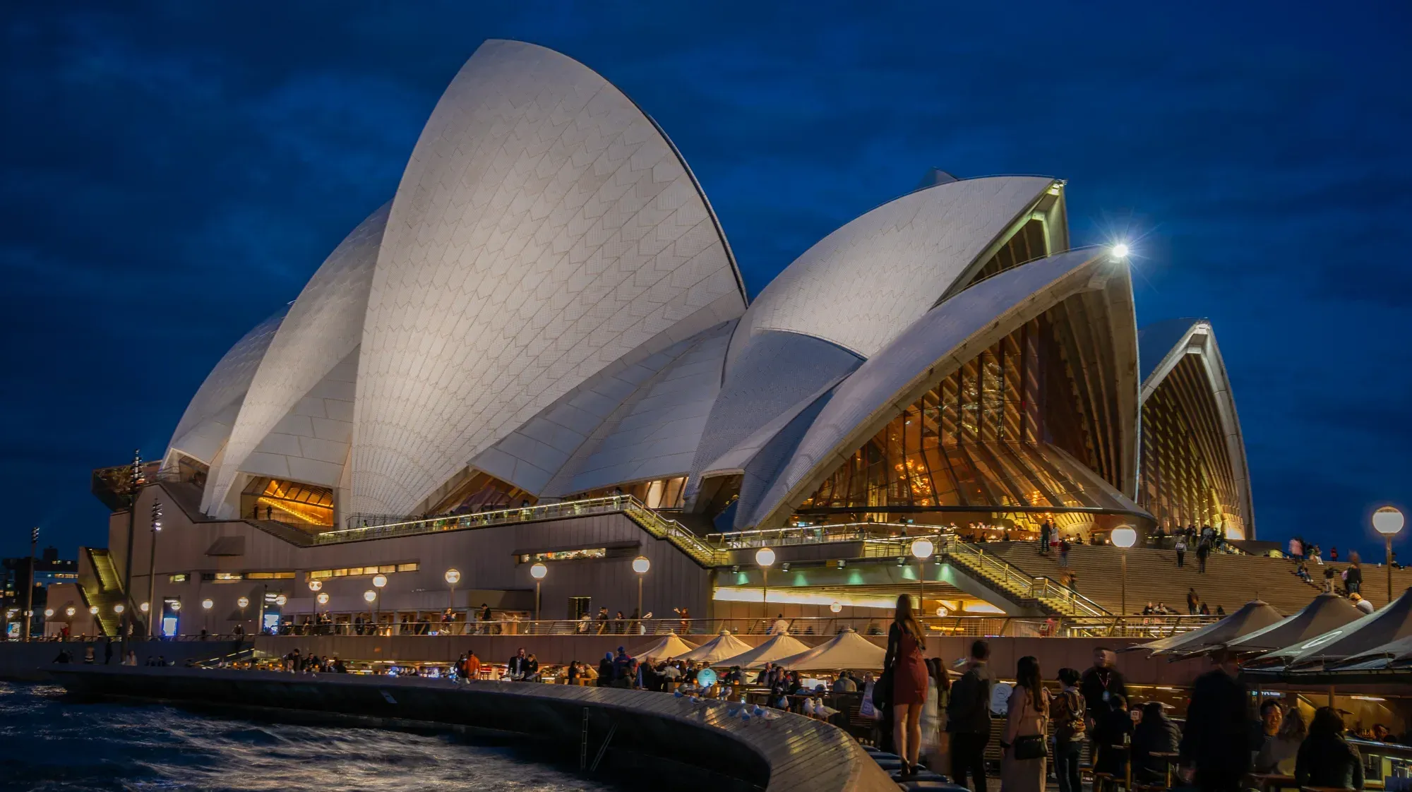 Sydney Opera House lit at dusk beside the harbour.