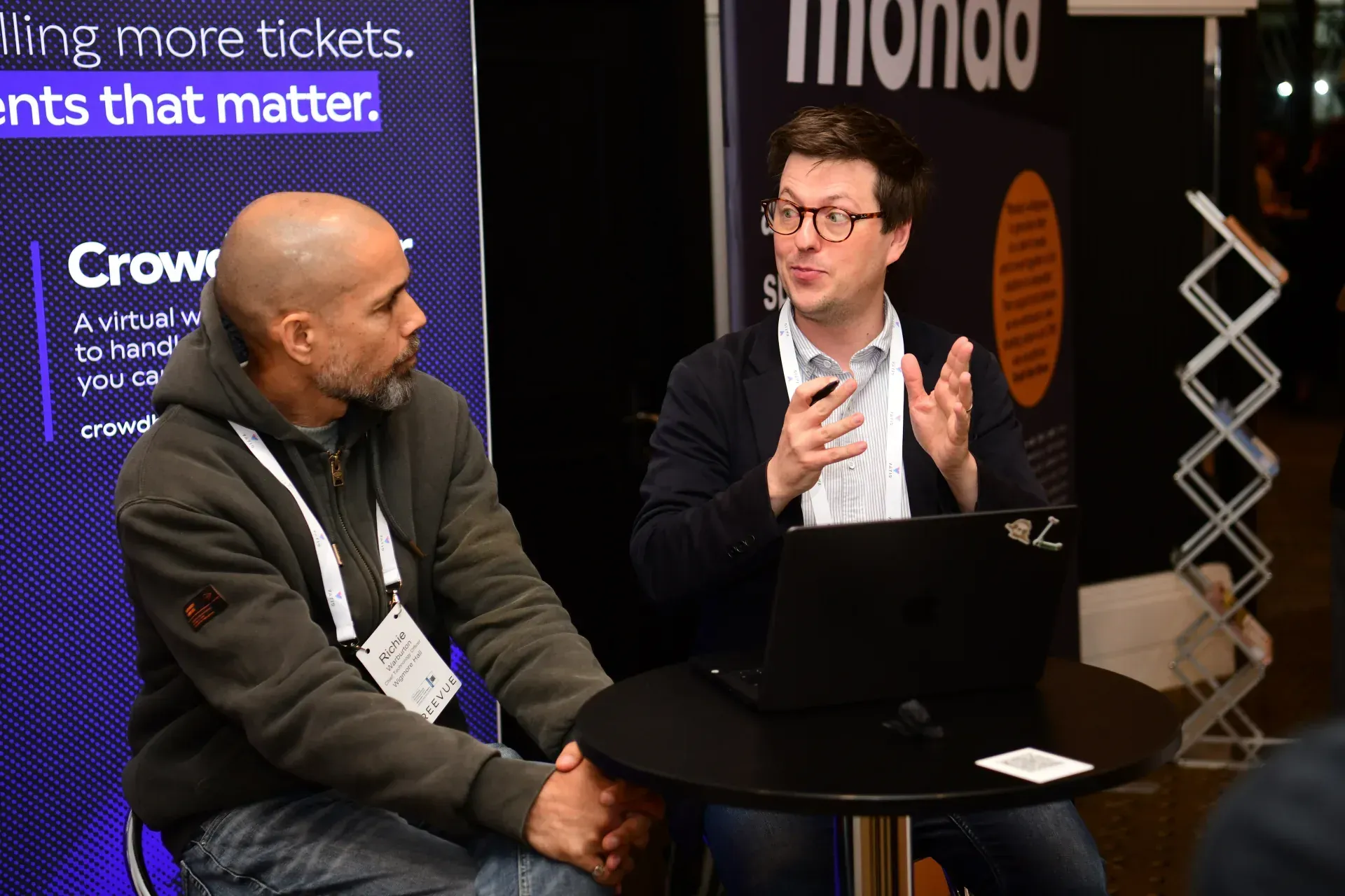 Two people talking at a Basker conference table in front of exhibitor banners.